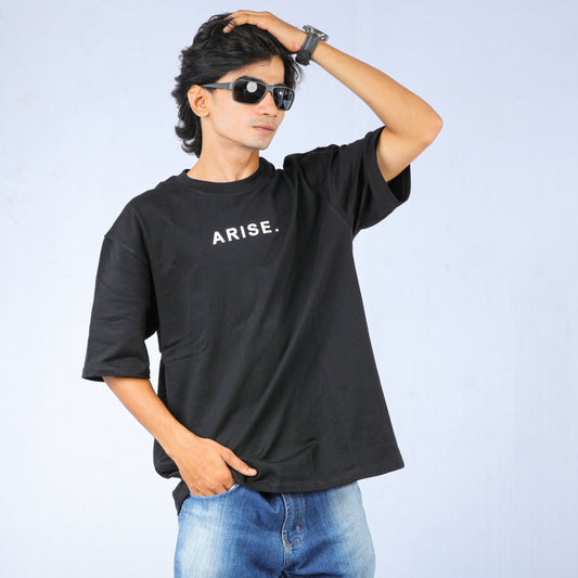 Person wearing a black t-shirt with 'ARISE.' text and blue jeans on a light gray background