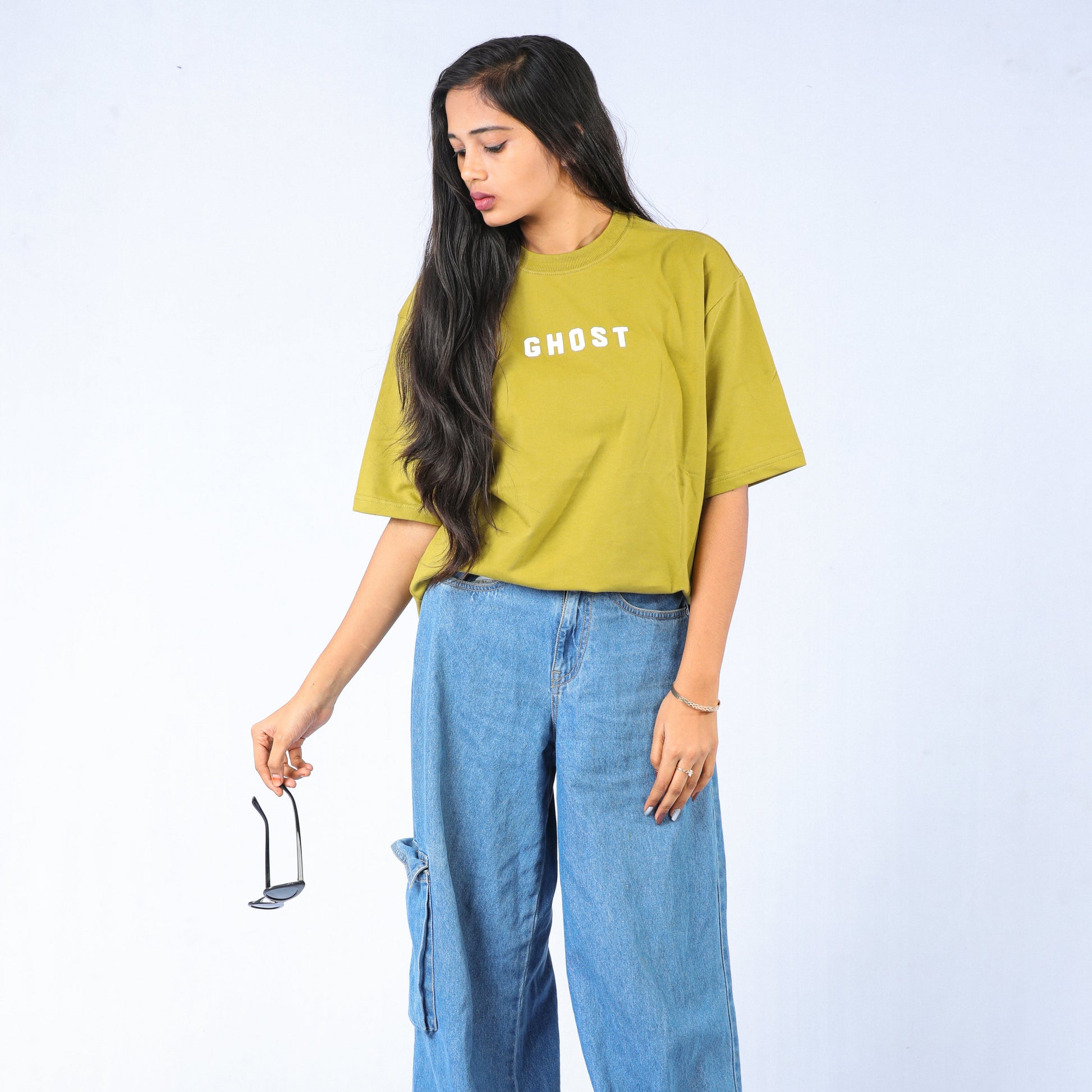 Woman wearing a yellow t-shirt with 'GHOST' text and blue jeans on a white background